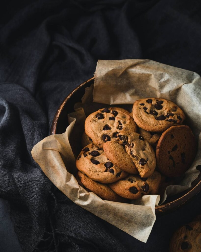 Chocolate chip cookies in a paper-lined basket on dark linen