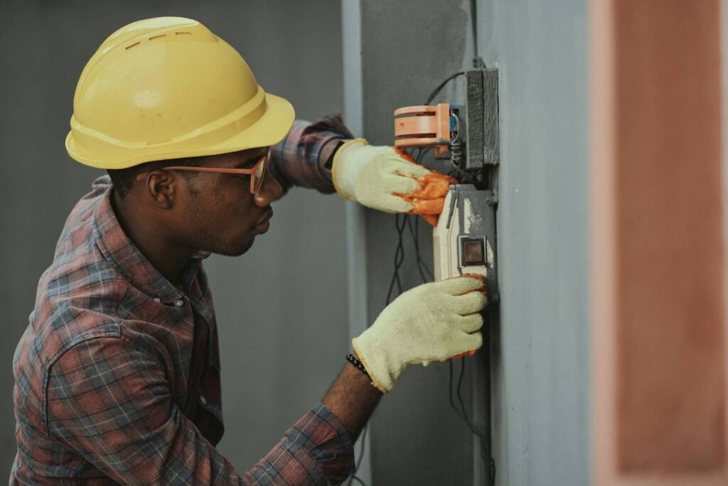 An electrician in a hard hat working on a wall-mounted panel