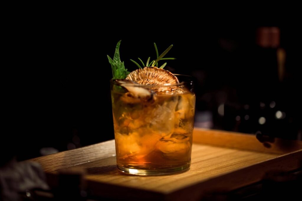 A whisky cocktail with a rosemary sprig on a dark wooden bar